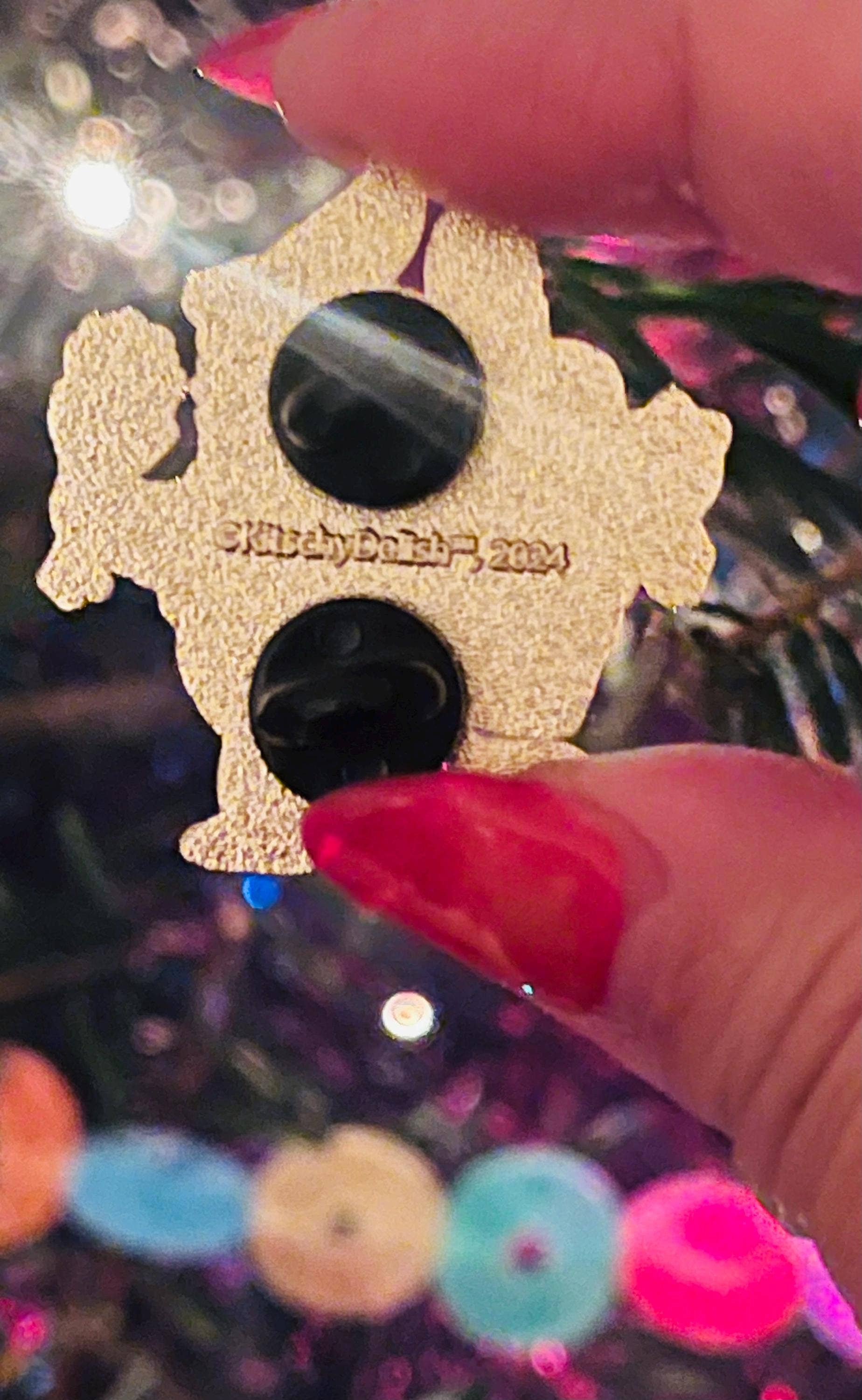 Gold and black decorative item held by a hand with red nail polish against a blurred background.