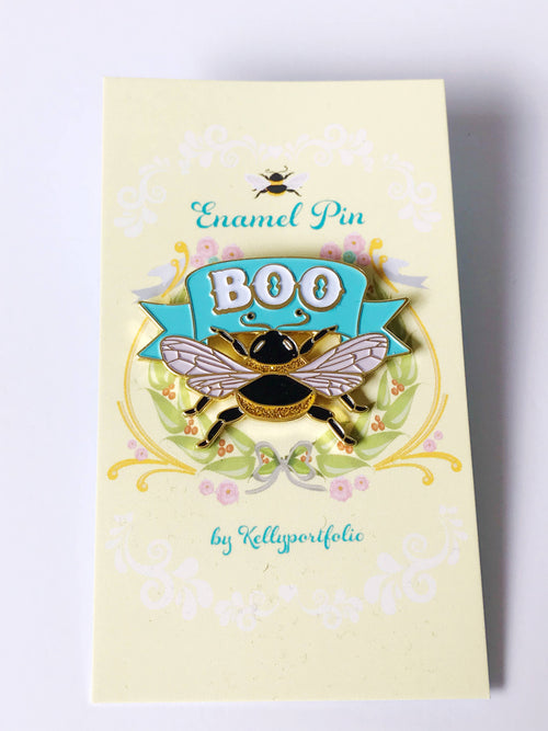 Enamel pin with bee design on a yellow card, featuring the word 'BOO' and 'Kellyporfolio' branding.