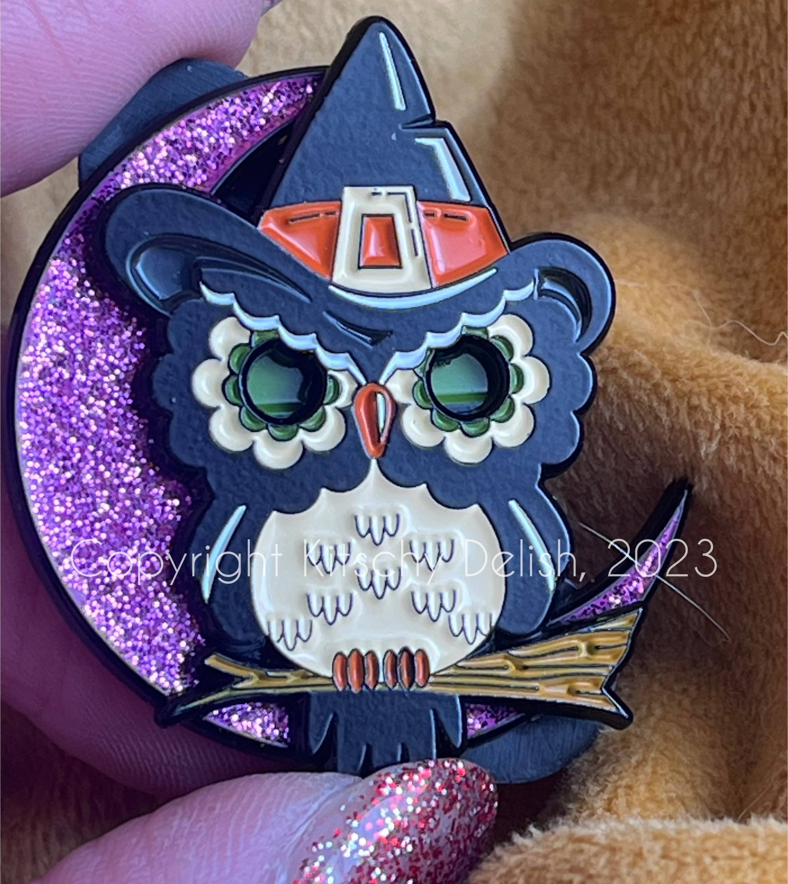 Halloween-themed owl pin with glittery purple base held by a hand.