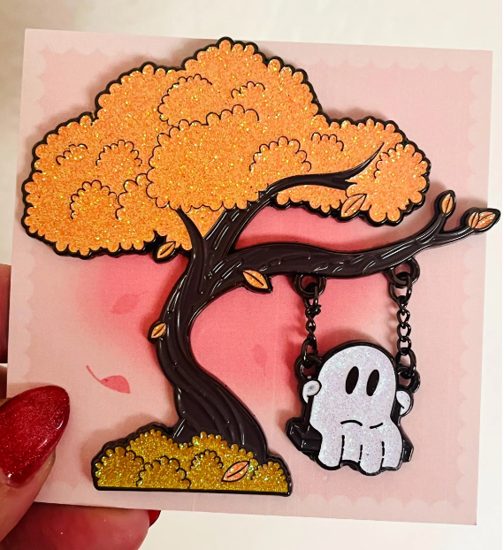 Tree-shaped brooch with a ghost charm on a pink background