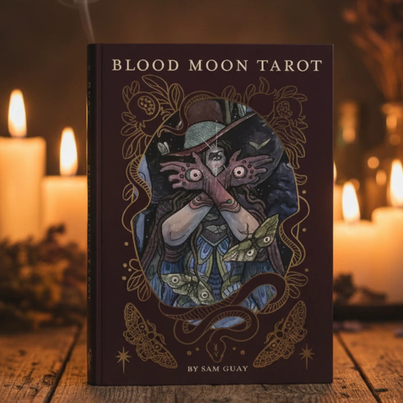 Book titled 'Blood Moon Tarot' with a cover illustration of a person with hands over eyes and decorative elements.