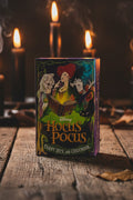 Disney Hocus Pocus card deck box standing on a rustic wooden table, surrounded by lit candles and smoke against a dark background.