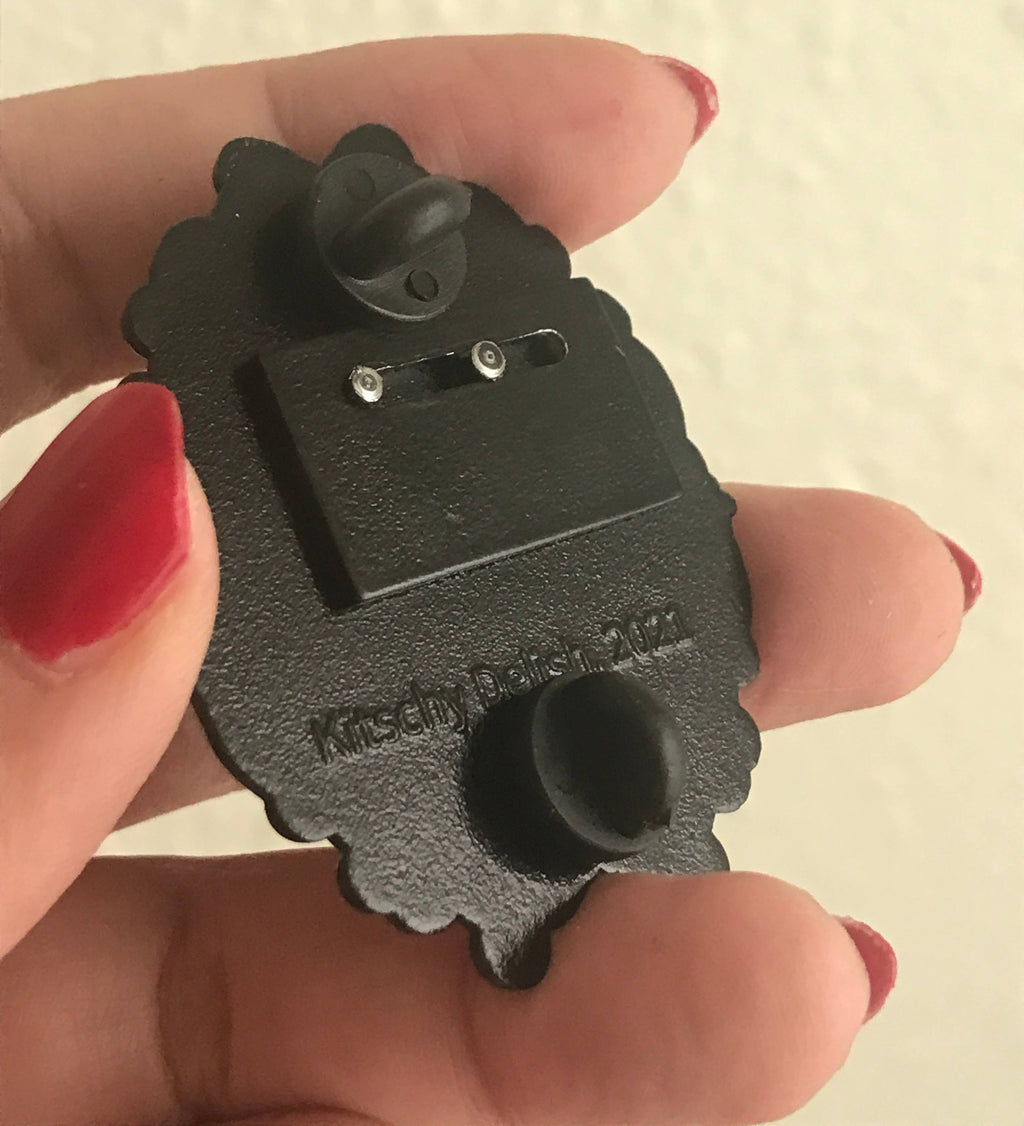 Black metal bracket held by a hand with red nail polish on a beige background