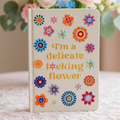 Notebook with floral designs and text on a soft surface with flowers in the background