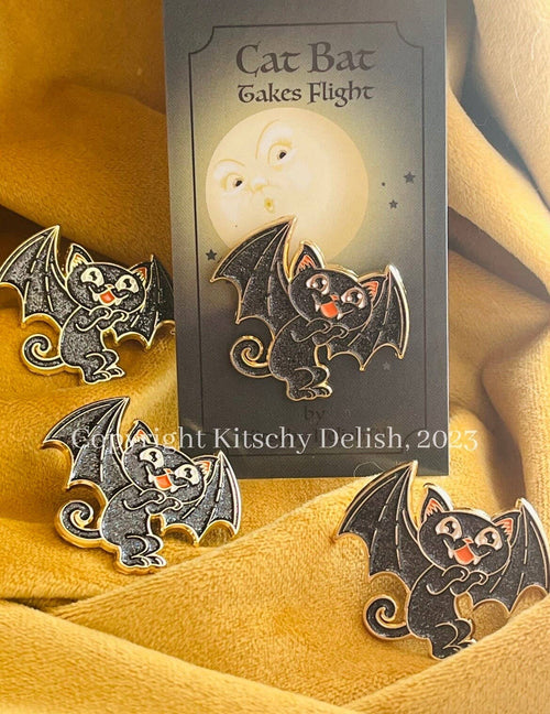 Cat bat pins with a card labeled 'Cat Bat Takes Flight' on a yellow fabric background.