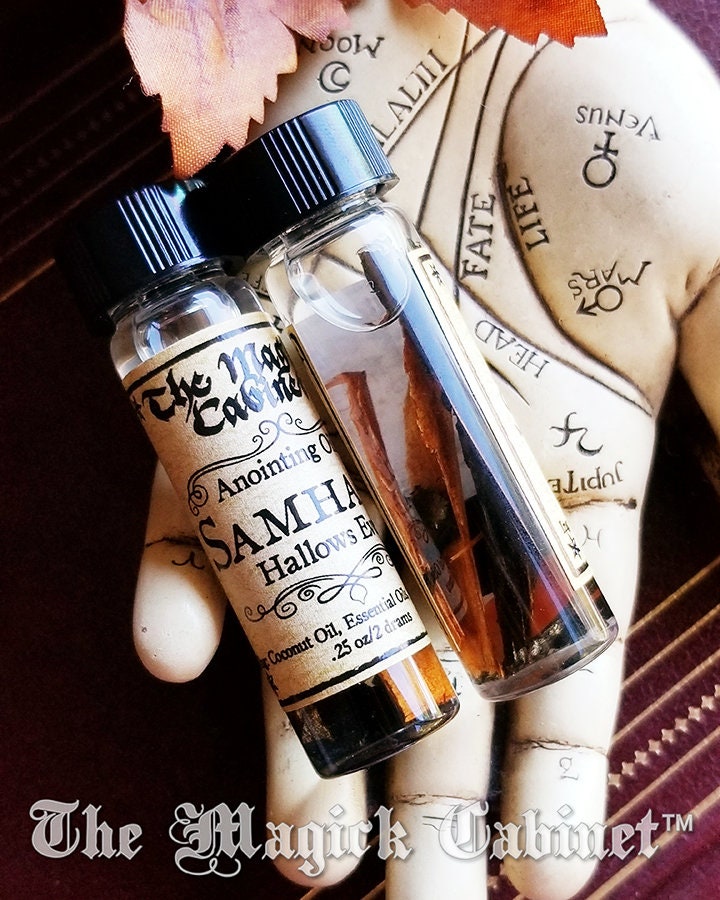 Two small bottles of 'Samhá Hallows Eve' oil from 'The Magick Cabinet' on a textured surface.